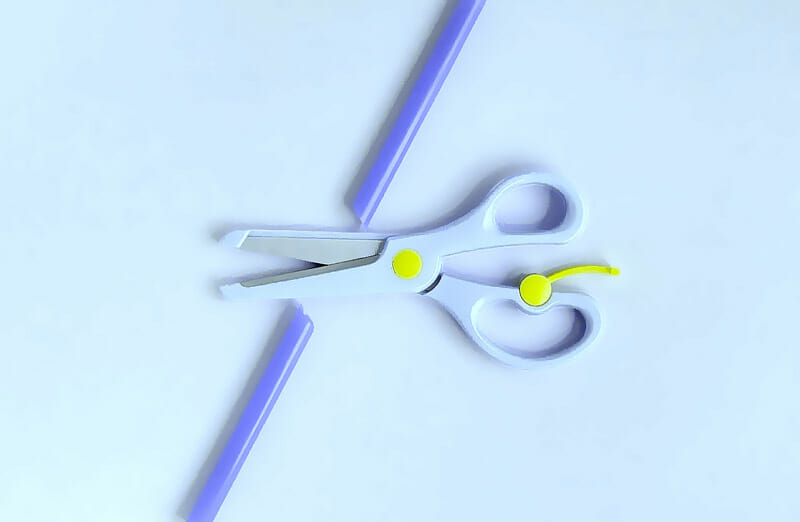 Imagem em fundo azul, com uma tesourinha infantil azul clara, cortando um canudinho azul escuro, representando de forma ilustrativa a vasectomia é um método cirúrgico contraceptivo realizado em homens.